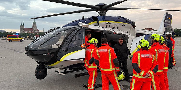 Polizeihubschrauber auf der Theresienwiese mit mehreren Flughelfern in leuchtend roten Einsatzkleidung und gelben Helmen