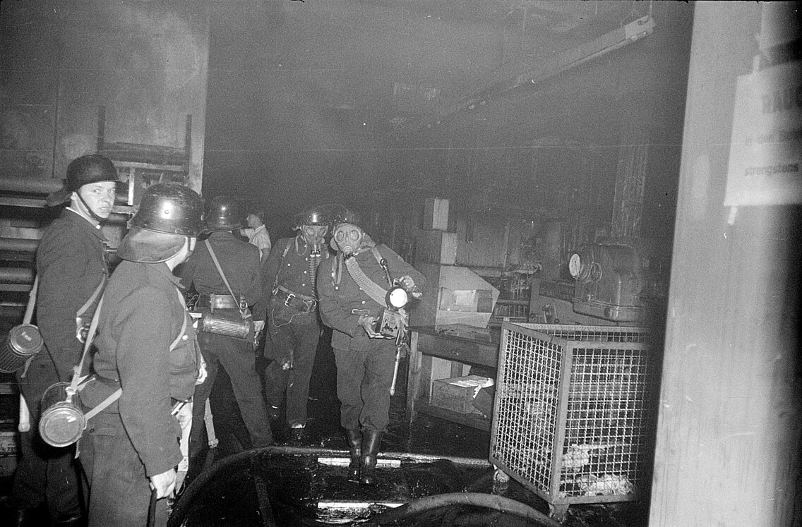 Kräfte der Berufsfeuerwehr mit Sauerstoffgeräten kommen vom Innenangriff in der Druckerei zurück 